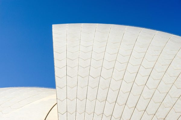 This image displays a curvilinear white structure with tile patterns against a clear blue sky, resembling a section of a modern architectural edifice.