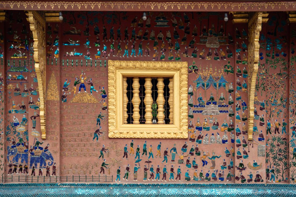 Intricate mural at Wat Xieng Thong in Laos depicting traditional scenes with people and animals, framed by a golden window, showcasing cultural heritage.