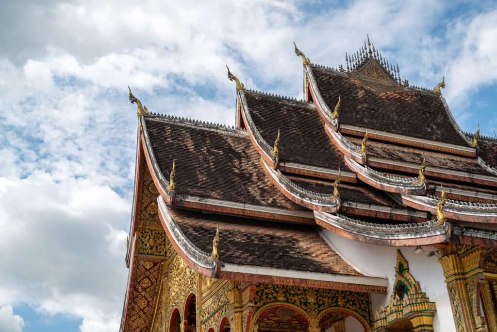 A traditional temple with ornate, multi-tiered roofs stands beneath a partly cloudy sky, showcasing intricate details and cultural architecture.