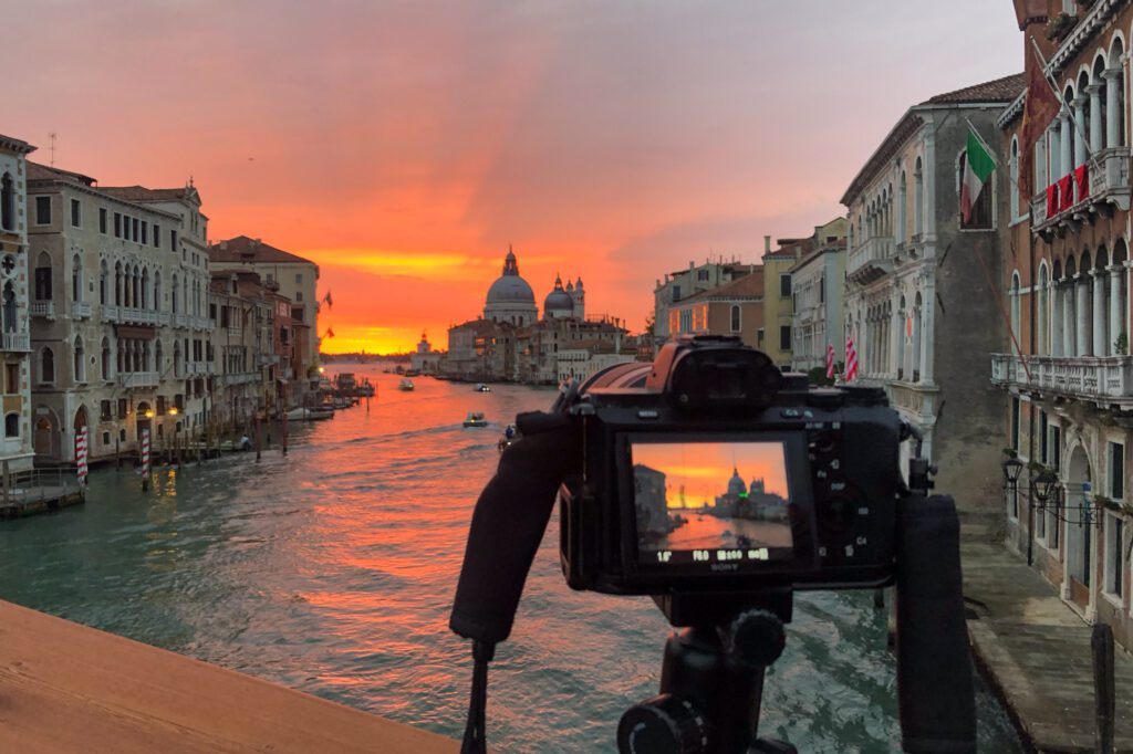 Travel photography tips - pack a tripod. Camera on tripod captures a sunset view of Venice's Grand Canal with the Basilica di Santa Maria della Salute visible in the background. 