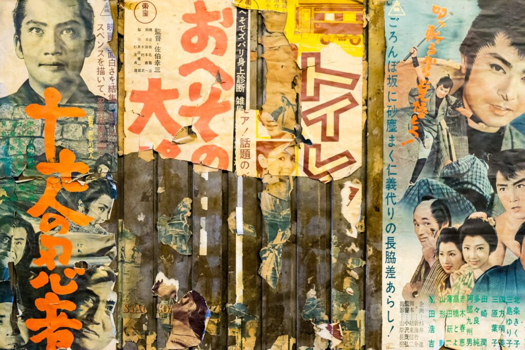 A collage of vintage Japanese movie posters featuring people, bold text, and traditional imagery. Torn and faded, showcasing retro film culture.