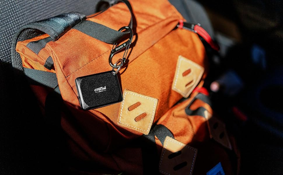 An orange backpack with leather accents sits on a car seat. A Cinegel-branded keychain is attached, illuminated by bright sunlight.